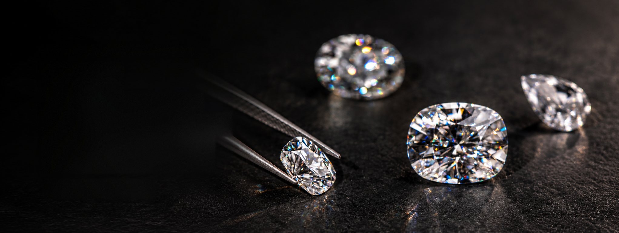 Diamantes de talla oval, cojín y pera sobre superficie negra, uno sostenido con pinzas