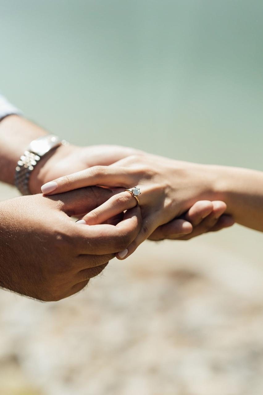 Pareja tomada de la mano; ella lleva un anillo de compromiso con diamante en oro amarillo